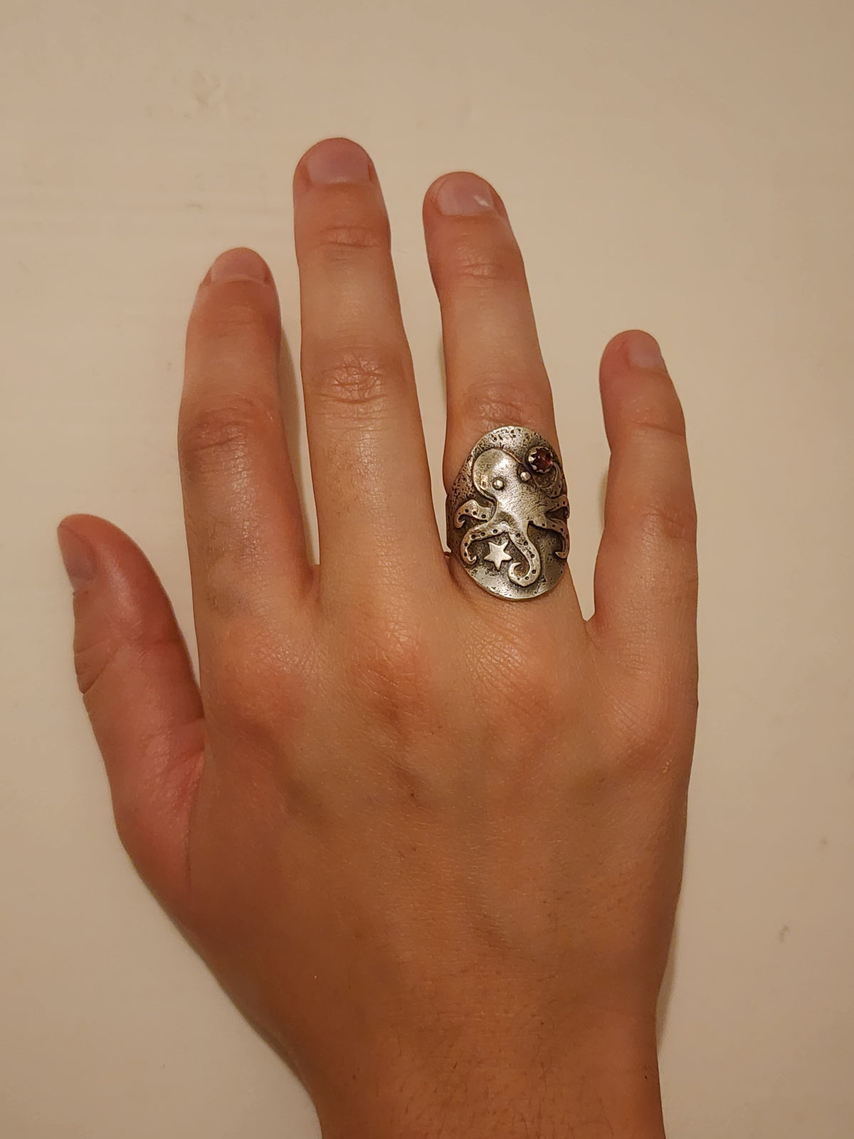 A sterling silver ring featuring an octopus design, shown worn on a person's ring finger against a plain beige background.