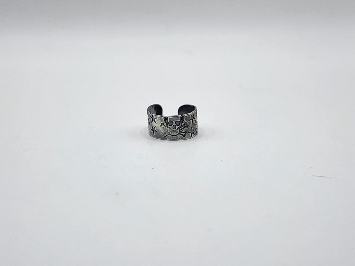 A sterling silver ear cuff earring with skull and crossbones and stars hand stamped and oxidized, photographed on a light background.