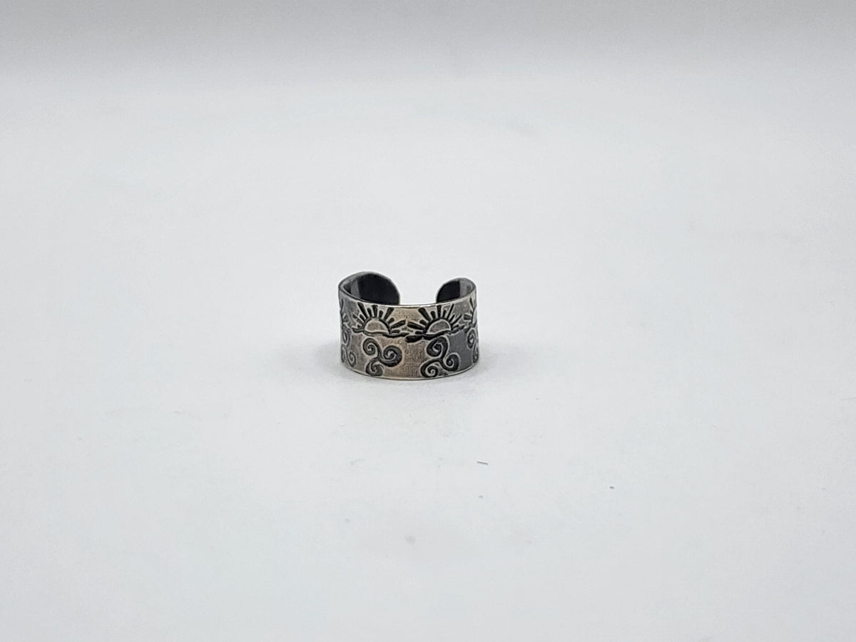 A sterling silver ear cuff with hand stamped suns and swirls and oxidized, photographed on a white background.