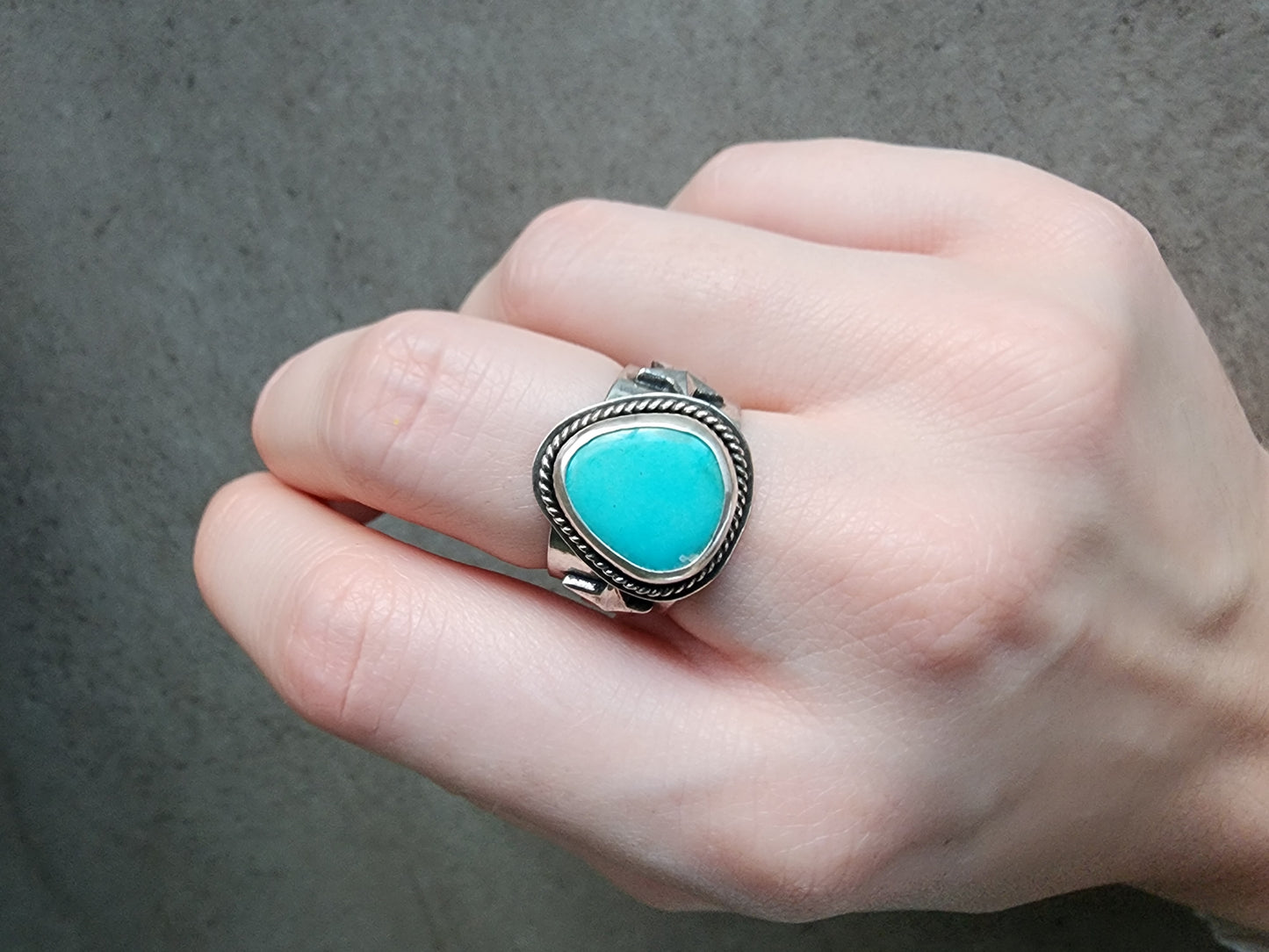 Hand wearing a turquoise stone ring with silver band on a neutral background