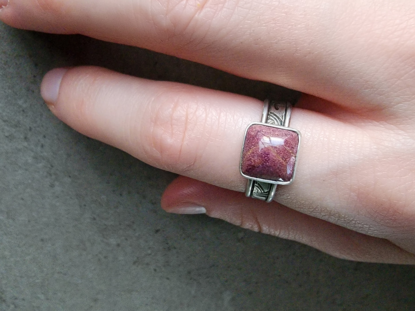 Hand wearing a ring with a stitchtite stone on a neutral background.