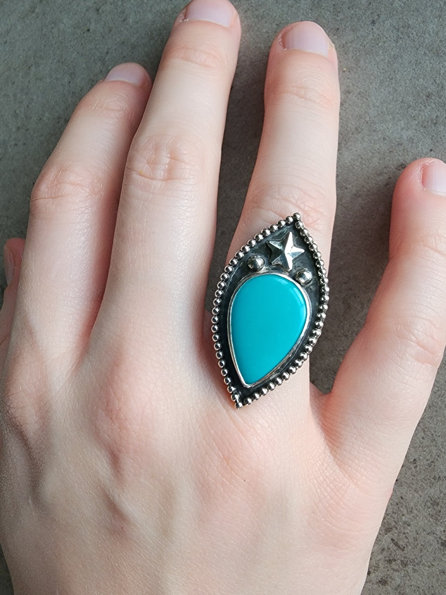 Turquoise ring with star, two silver balls and border with silver band on a hand against a neutral background