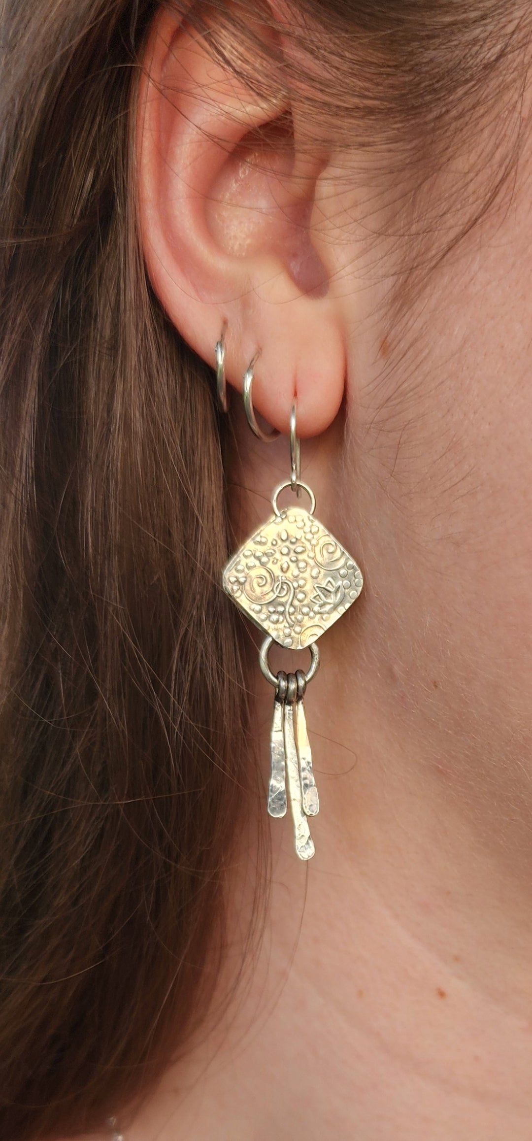 Close-up of a person wearing sterling silver earring with dangling elements.