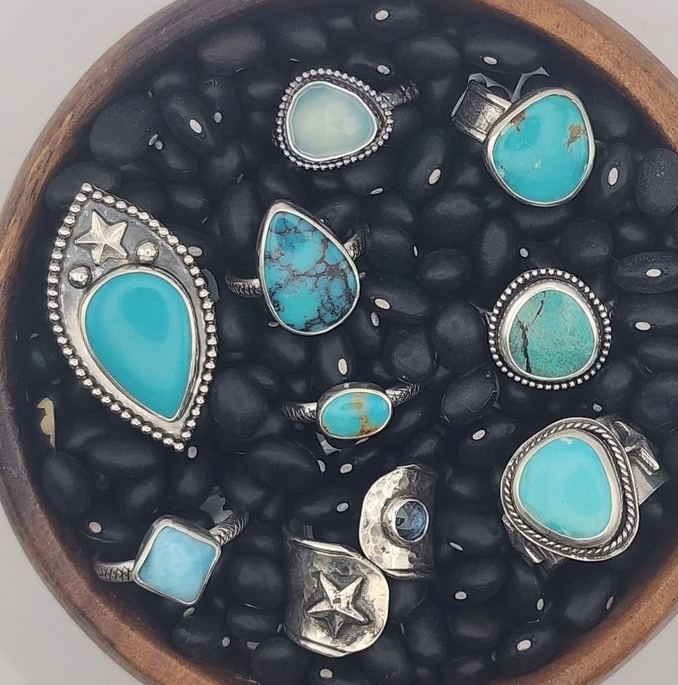 Wooden bowl with black beans with nine rings with blue stones sitting on a white background. 