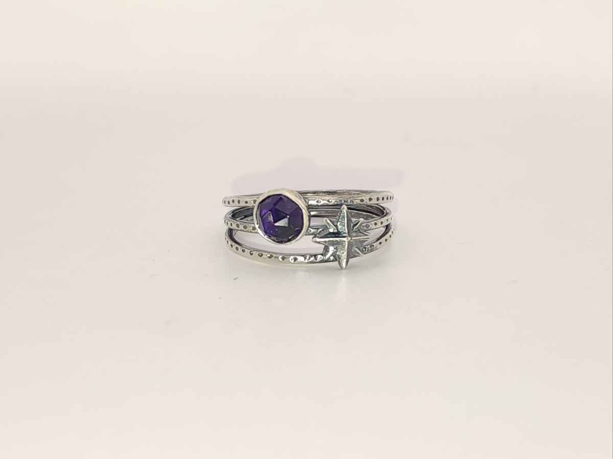 A sterling silver ring with a round amethyst and a star accent on a three band ring with texture, photographed on a plain light background.