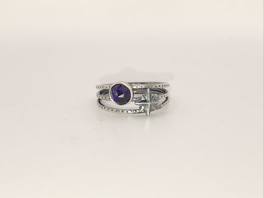 A sterling silver ring with a round amethyst and a star accent on a three band ring with texture, photographed on a plain light background.