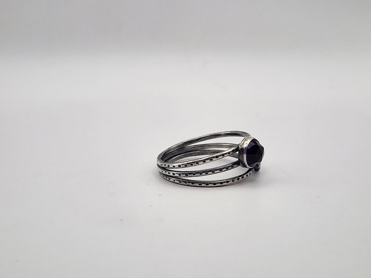 A sterling silver ring with a round amethyst on a three band ring with texture, photographed on a plain light background.