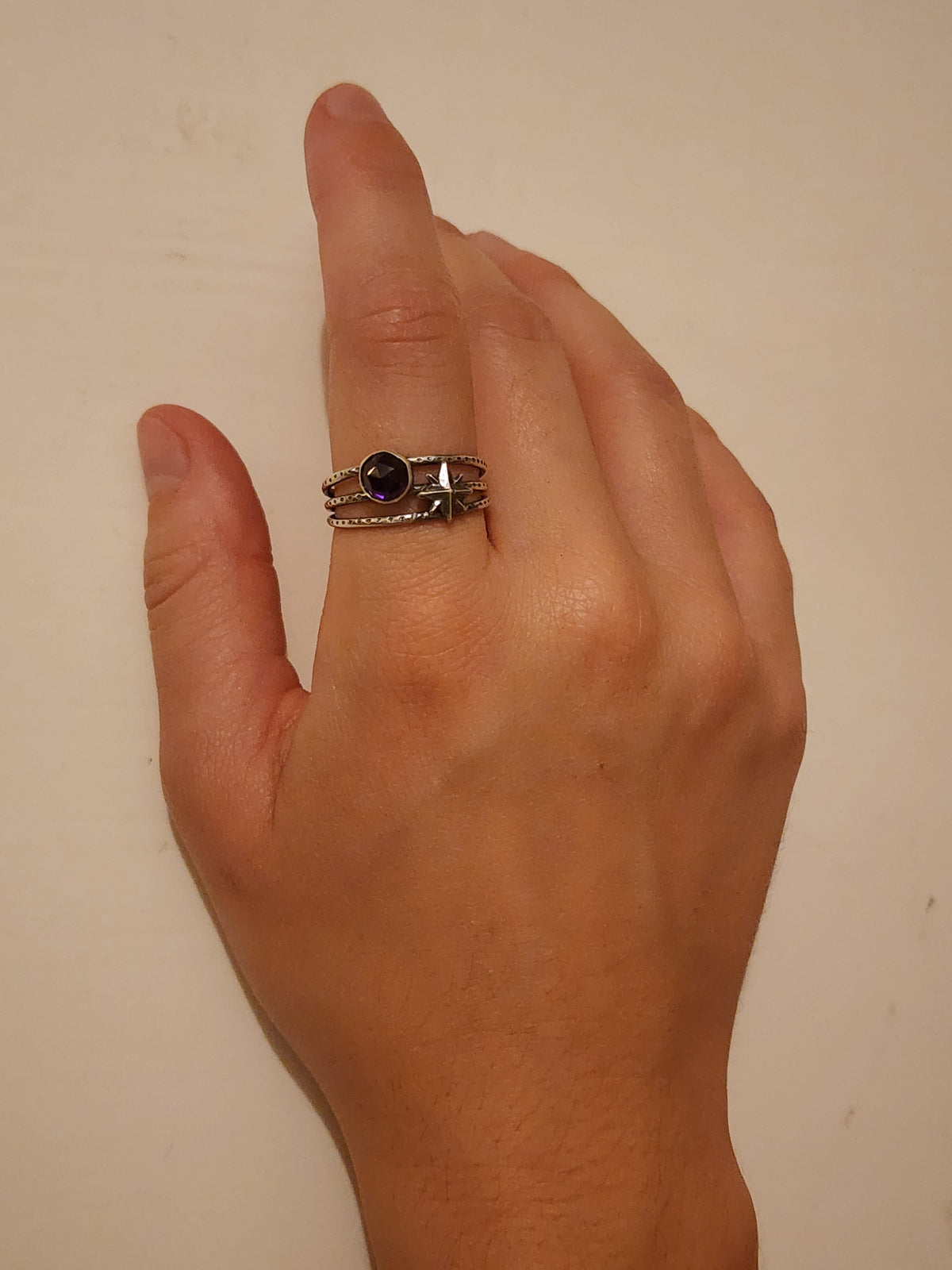 A sterling silver ring with a dark round gemstone and a small star detail, worn on a person's pointer finger against a plain beige background.