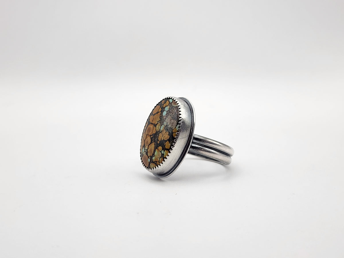 A sterling silver ring featuring a large oval cabochon stone with a mottled pattern of orange, brown, and turquoise on a double ring band, set against a clean white background.