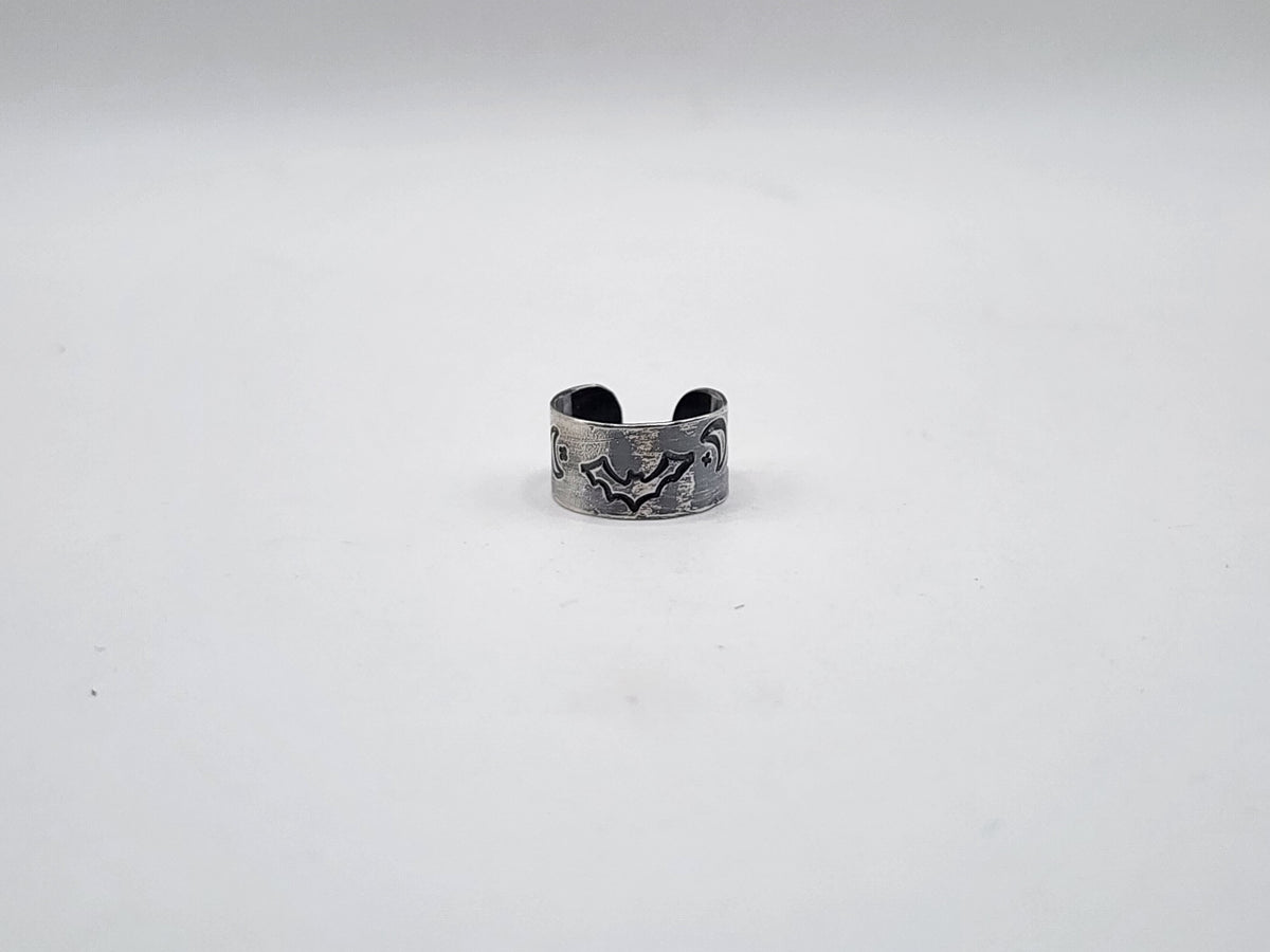 A sterling silver cuff earring with a hand-stamped bat, star and crescent moon design on the front, displayed on a plain light gray background.