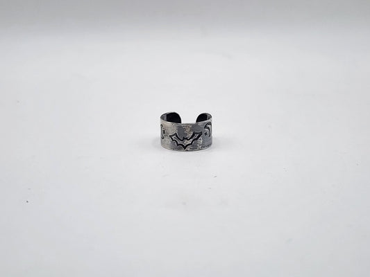A sterling silver cuff earring with a hand-stamped bat, star and crescent moon design on the front, displayed on a plain light gray background.