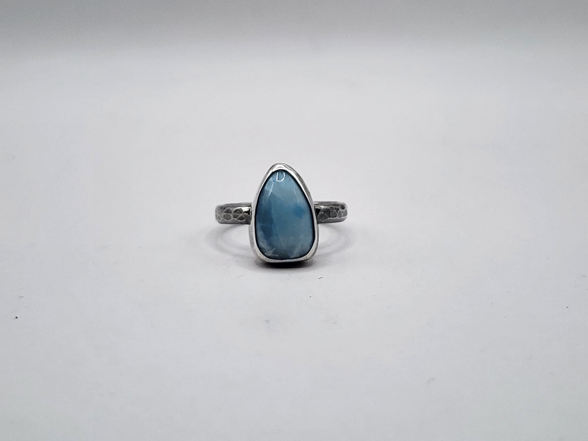 A sterling silver ring featuring a teardrop-shaped light blue gemstone on a hammer textured ring band, set against a plain light gray background.