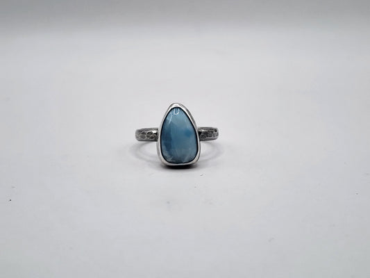 A sterling silver ring featuring a teardrop-shaped light blue gemstone on a hammer textured ring band, set against a plain light gray background.