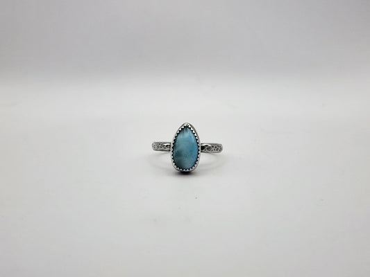 A sterling silver ring with teardrop blue stone and serrated bezel set on a hammer textured ring and oxidized, photographed on a white/light grey background. 