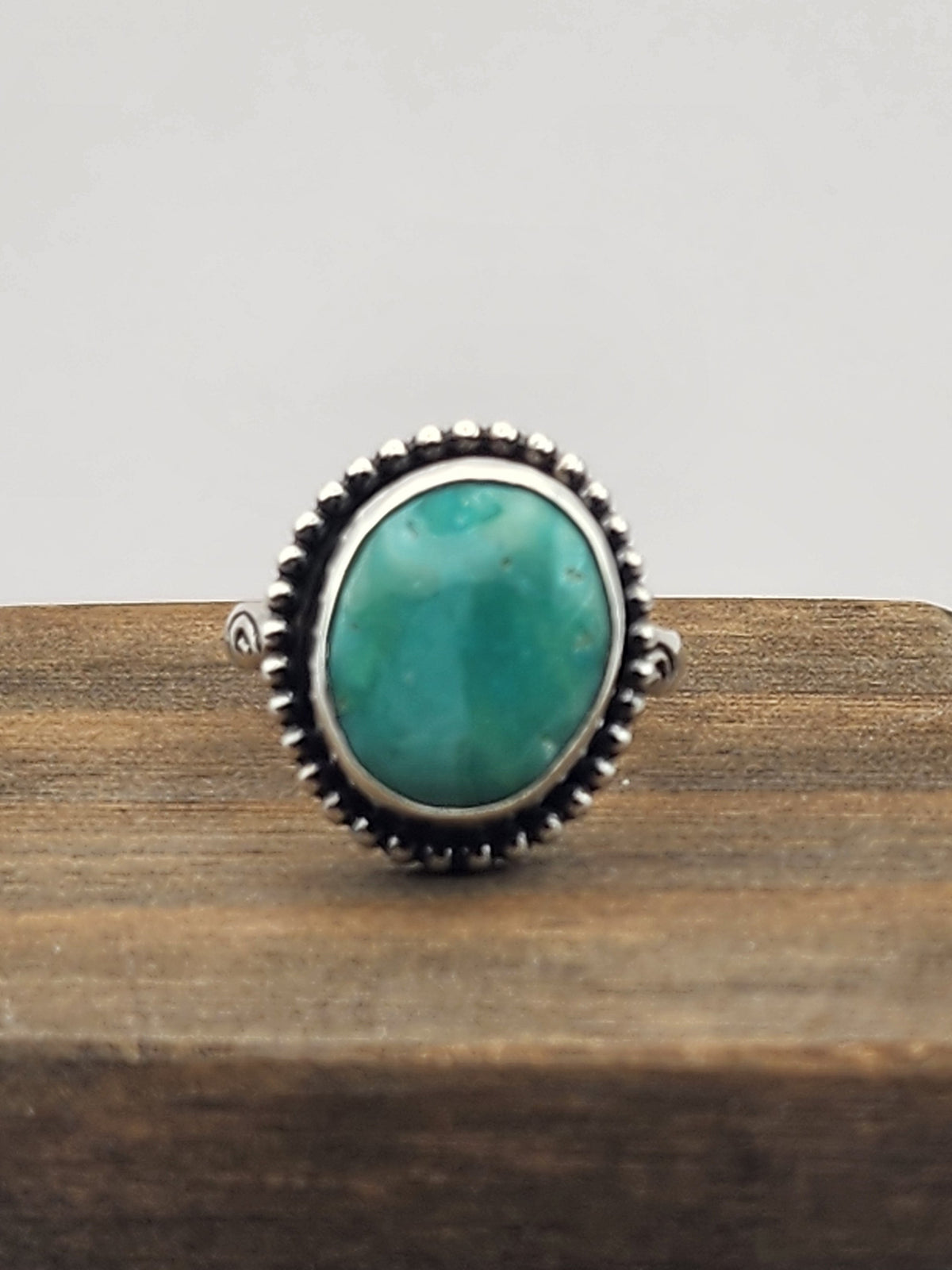 Turquoise ring with sterling silver beaded border and stamped band sitting on wood with a white background.