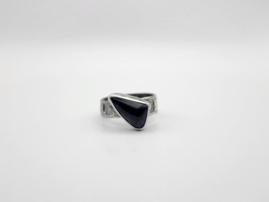 A sterling silver ring with a irregular triangular dark stone offset on a textured band, photographed on a white background. 