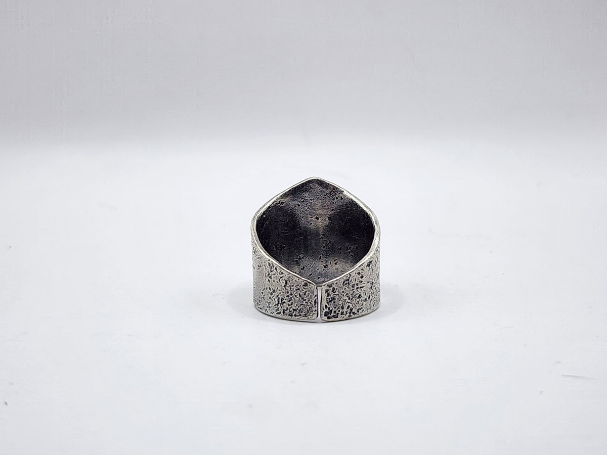A textured sterling silver ring with a unique shield-like or teardrop-shaped top, pictured from the back side showing an open ring shank, photographed on a plain white background.