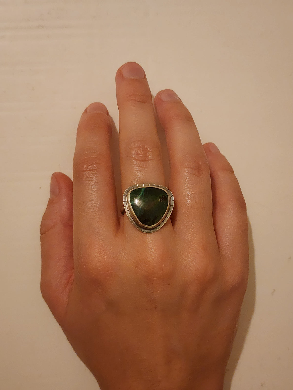 A sterling silver ring featuring a large, polished green teardrop/triangular-shaped gemstone, shown worn on a person's middle finger against a plain off-white background.