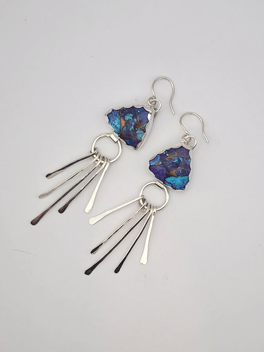 A pair of sterling silver dangle earrings featuring triangular shaped blue and purple mohave turquoise stone pendants with sterling silver fringe, displayed on a neutral light gray background.