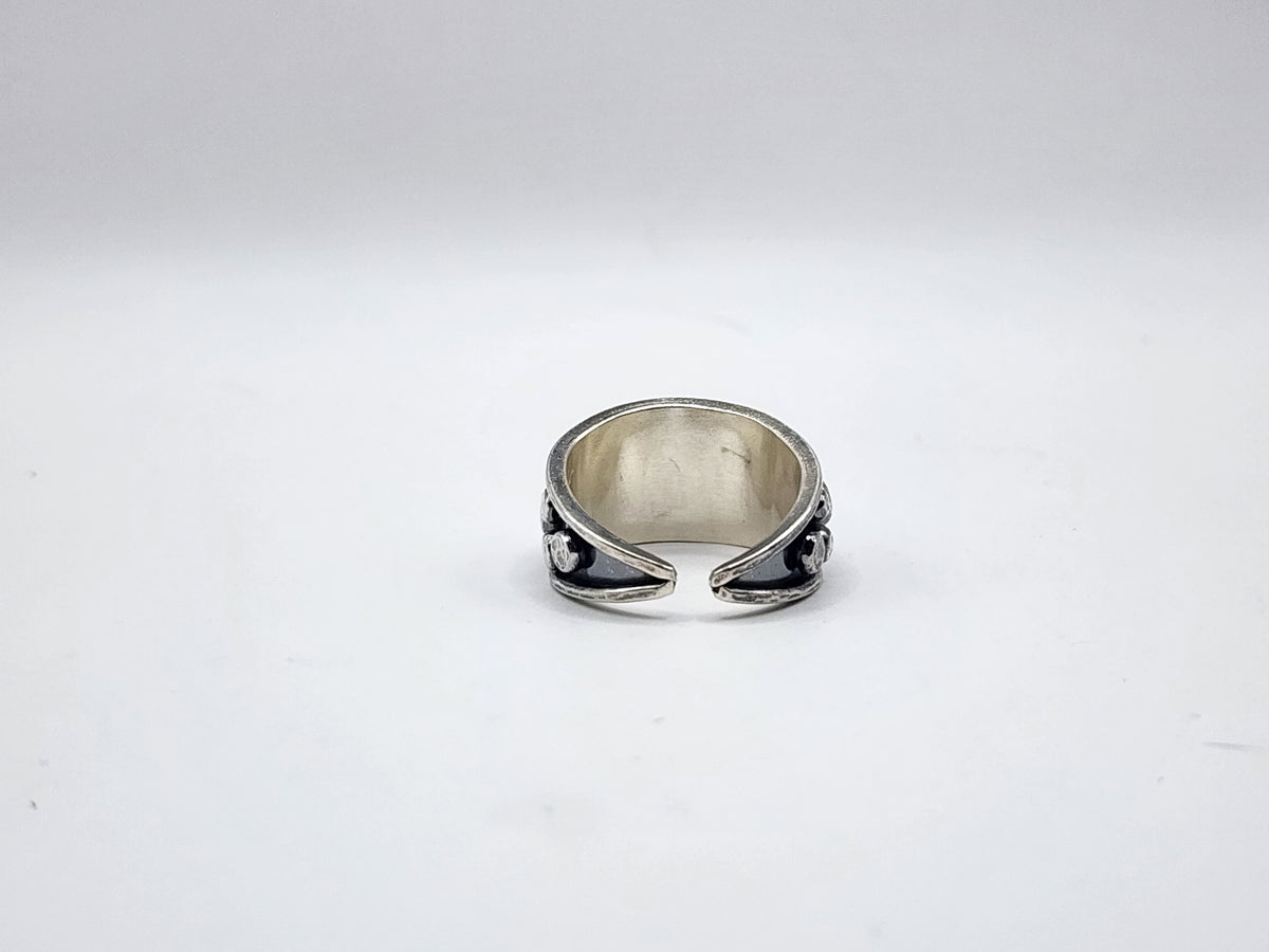 A sterling silver split ring pictured from the back side to show open band, with silver dots on side and heavy oxidation, photographed on a plain white background.