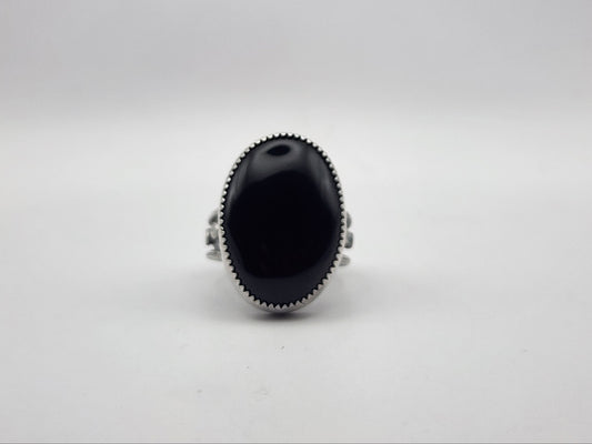 A sterling silver ring featuring a large, oval-shaped black onyx cabochon stone, photographed against a neutral light gray background.