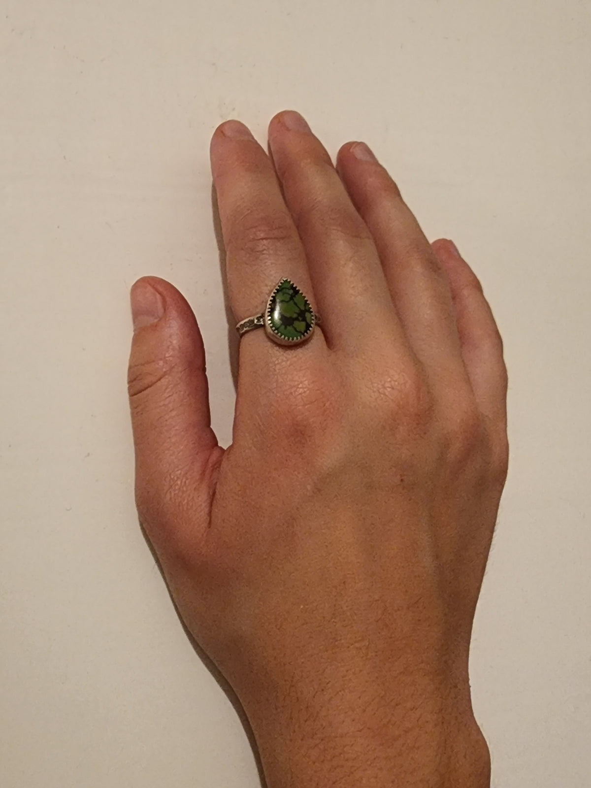 A sterling silver ring with a green turquoise teardrop-shaped stone with natural dark veining, worn on the pointer finger of a hand against a plain off-white background.