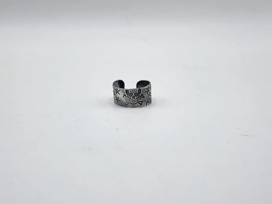 A sterling silver ear cuff earring with skull and crossbones and stars hand stamped and oxidized, photographed on a light background.