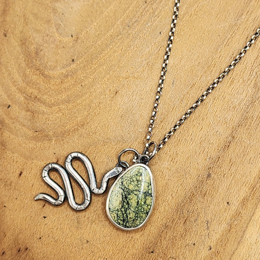 A sterling silver snake-shaped pendant necklace with a green marbled teardrop stone pendant, displayed on a light brown wooden surface.