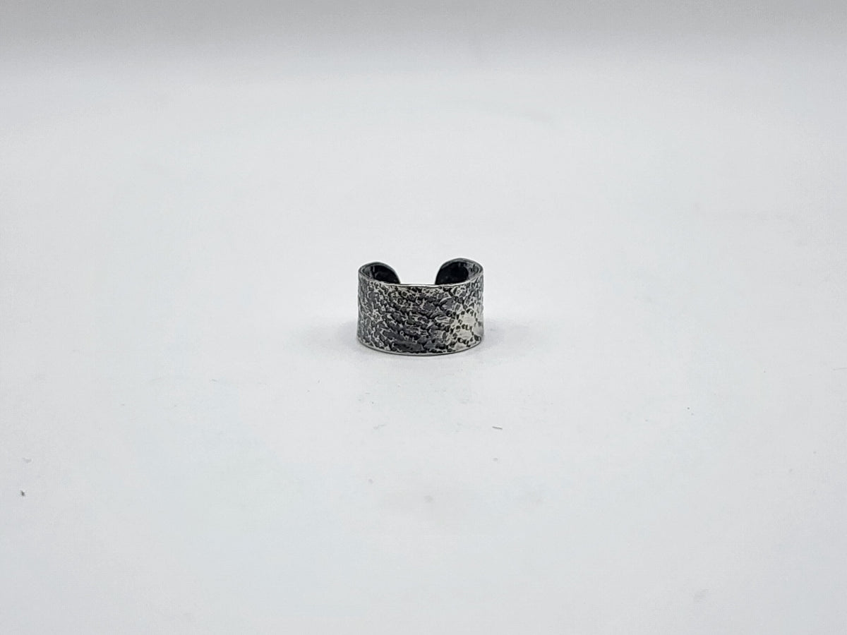 A sterling silver ear cuff with a snake like texture and heavily oxidized, photographed on a white background.