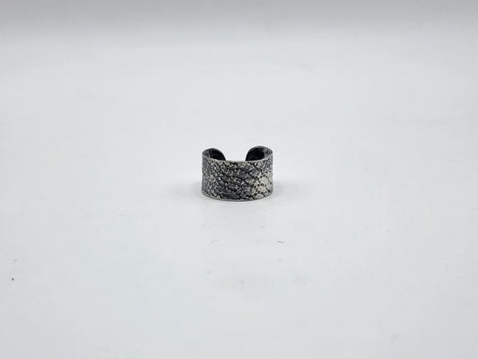 A sterling silver ear cuff with a snake like texture and heavily oxidized, photographed on a white background.