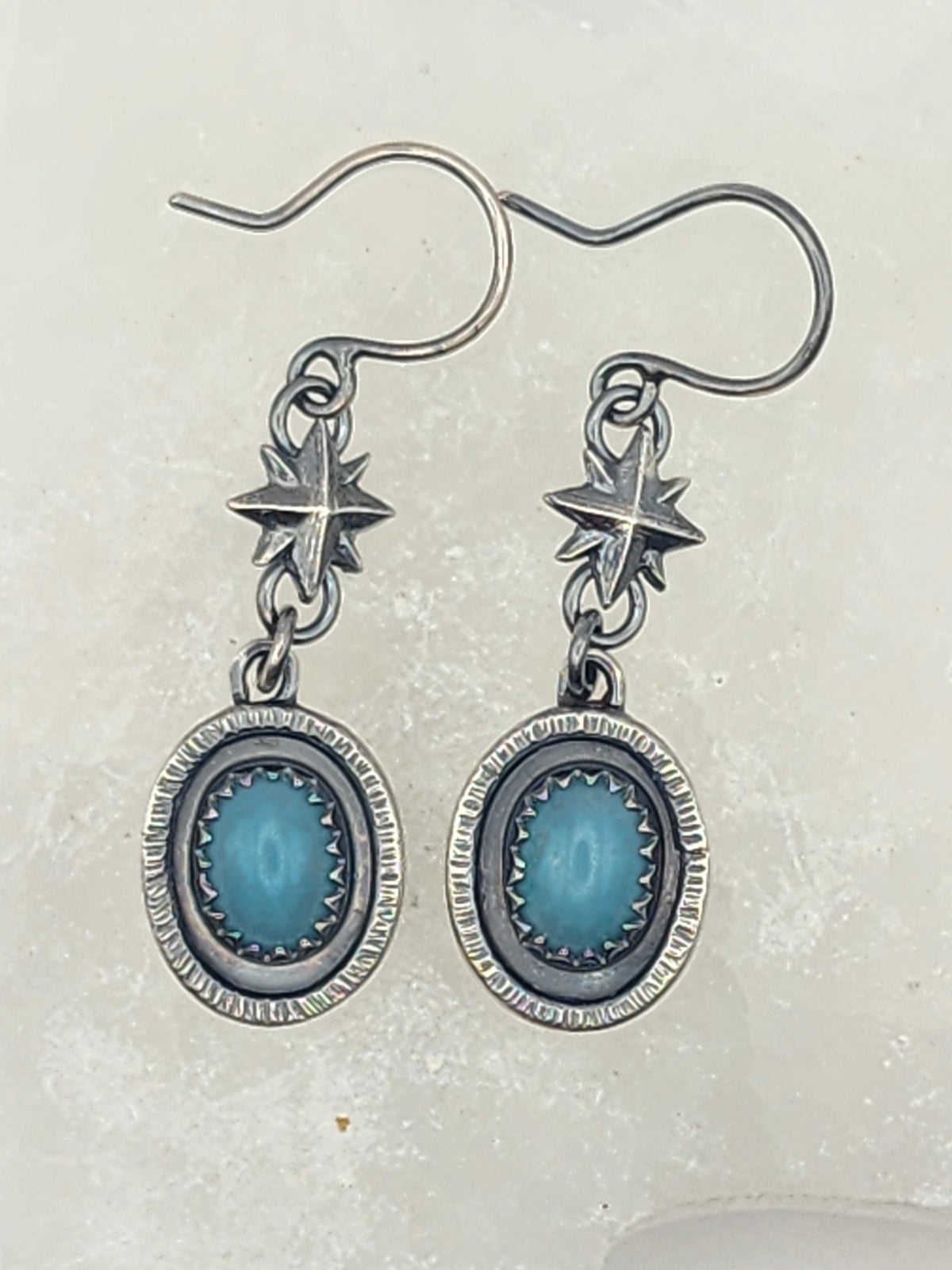 A pair of sterling silver dangle earrings with oval amazonite stone centers and star-shaped components, shown on a light textured background.