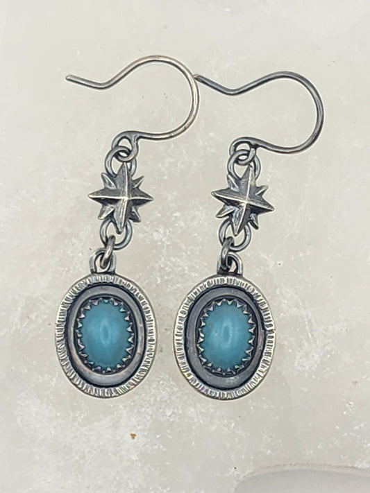 A pair of sterling silver dangle earrings with oval amazonite stone centers and star-shaped components, shown on a light textured background.