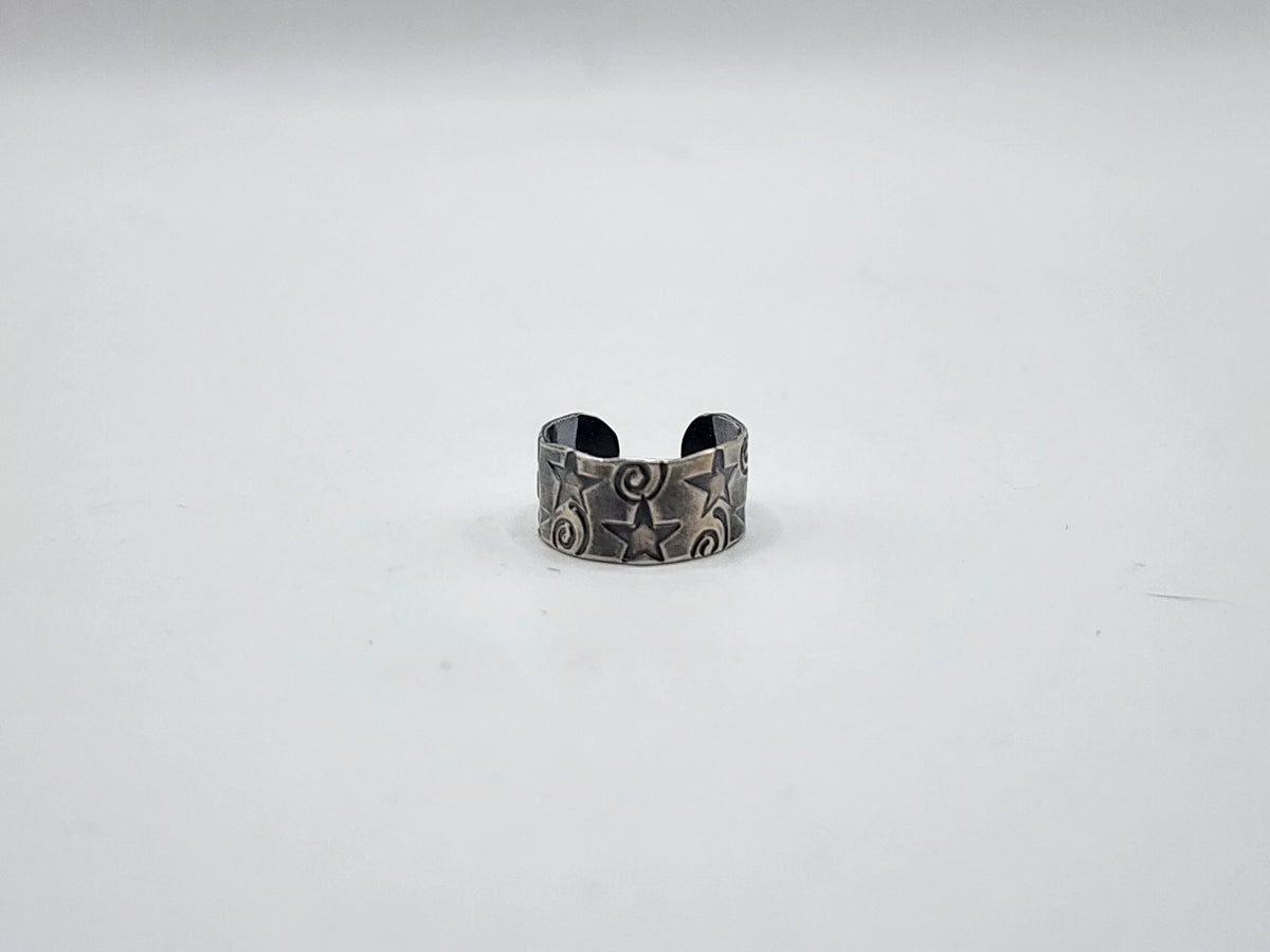 A sterling silver ear cuff with hand stamped stars and swirls and heavily oxidized, photographed on a plain white background.