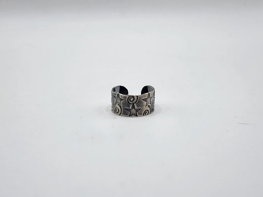 A sterling silver ear cuff with hand stamped stars and swirls and heavily oxidized, photographed on a plain white background.