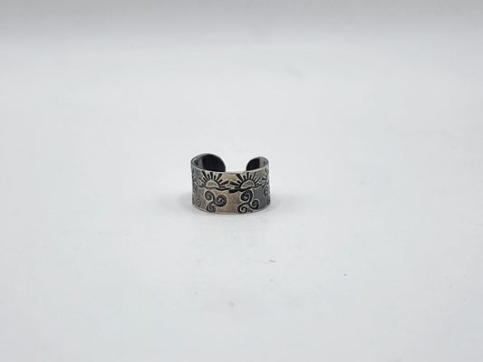 A sterling silver ear cuff with hand stamped suns and swirls and oxidized, photographed on a white background.