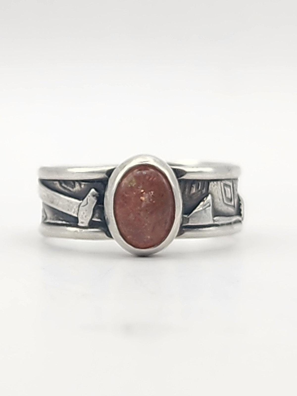 A sterling silver ring with heavily textured band and round orange stone in the center on a white background. 