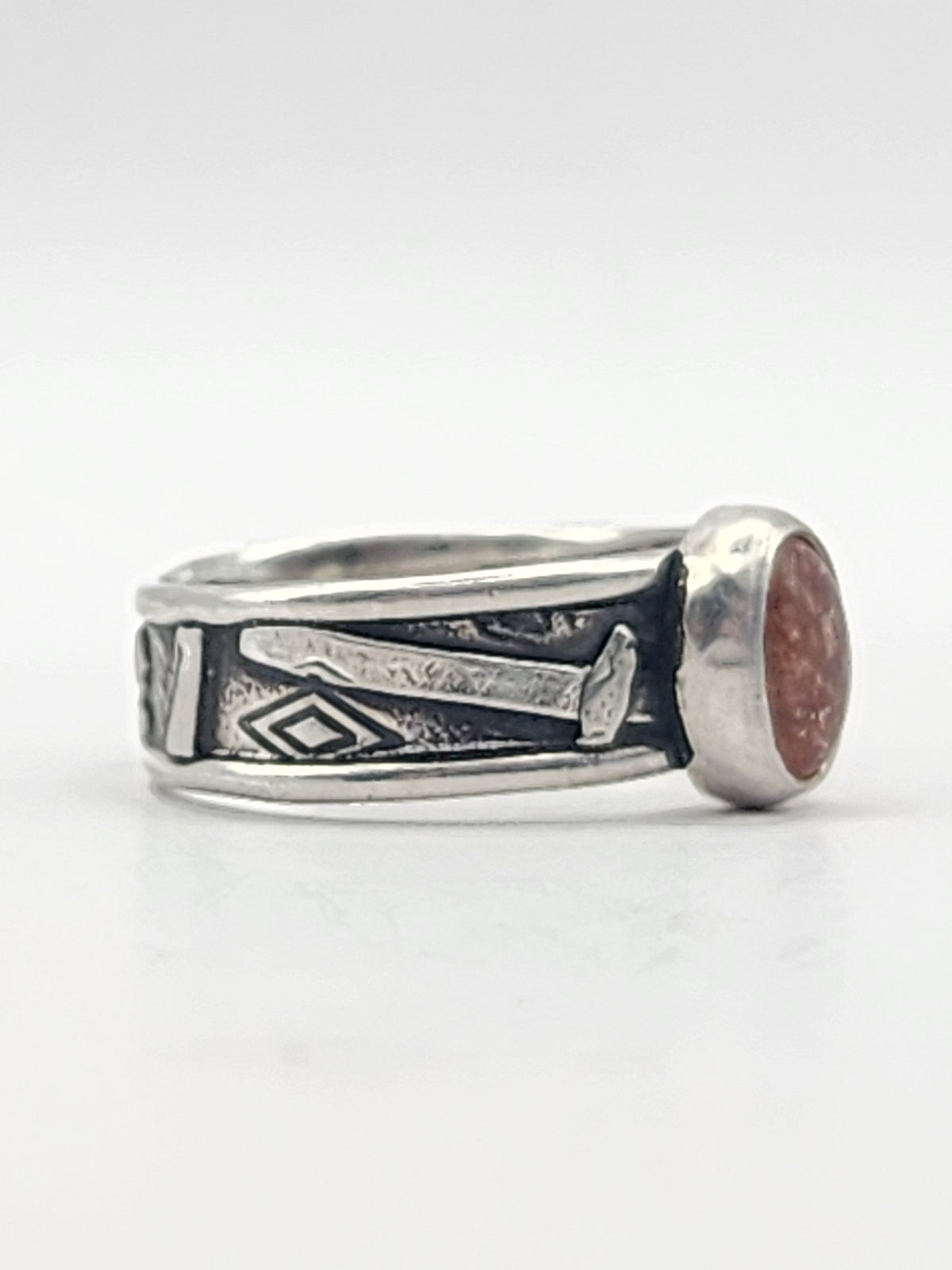 A side view of a sterling silver ring with heavily textured band and round orange stone in the center on a white background. 