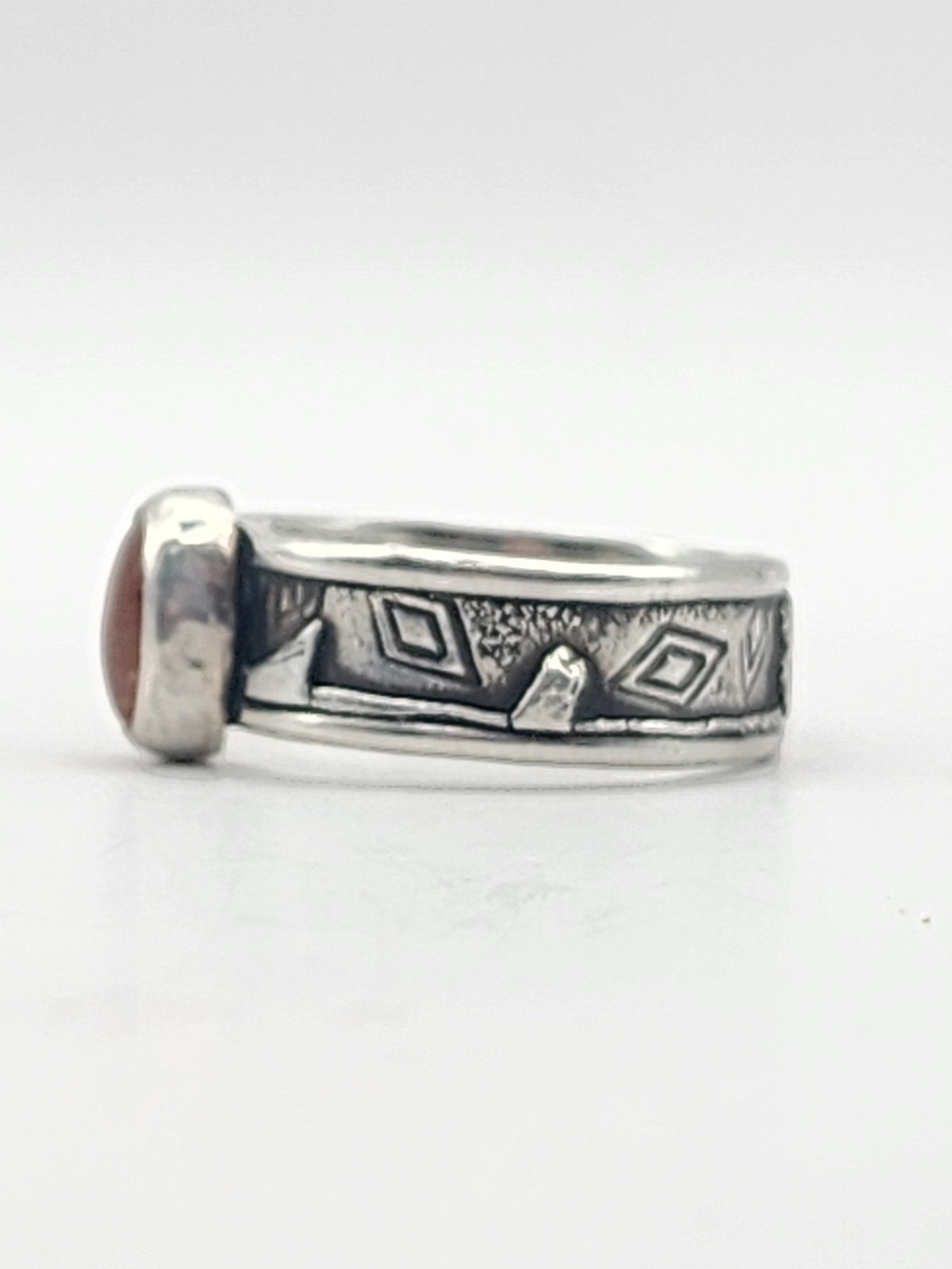 A side view of a sterling silver ring with heavily textured band and round orange stone in the center on a white background. 