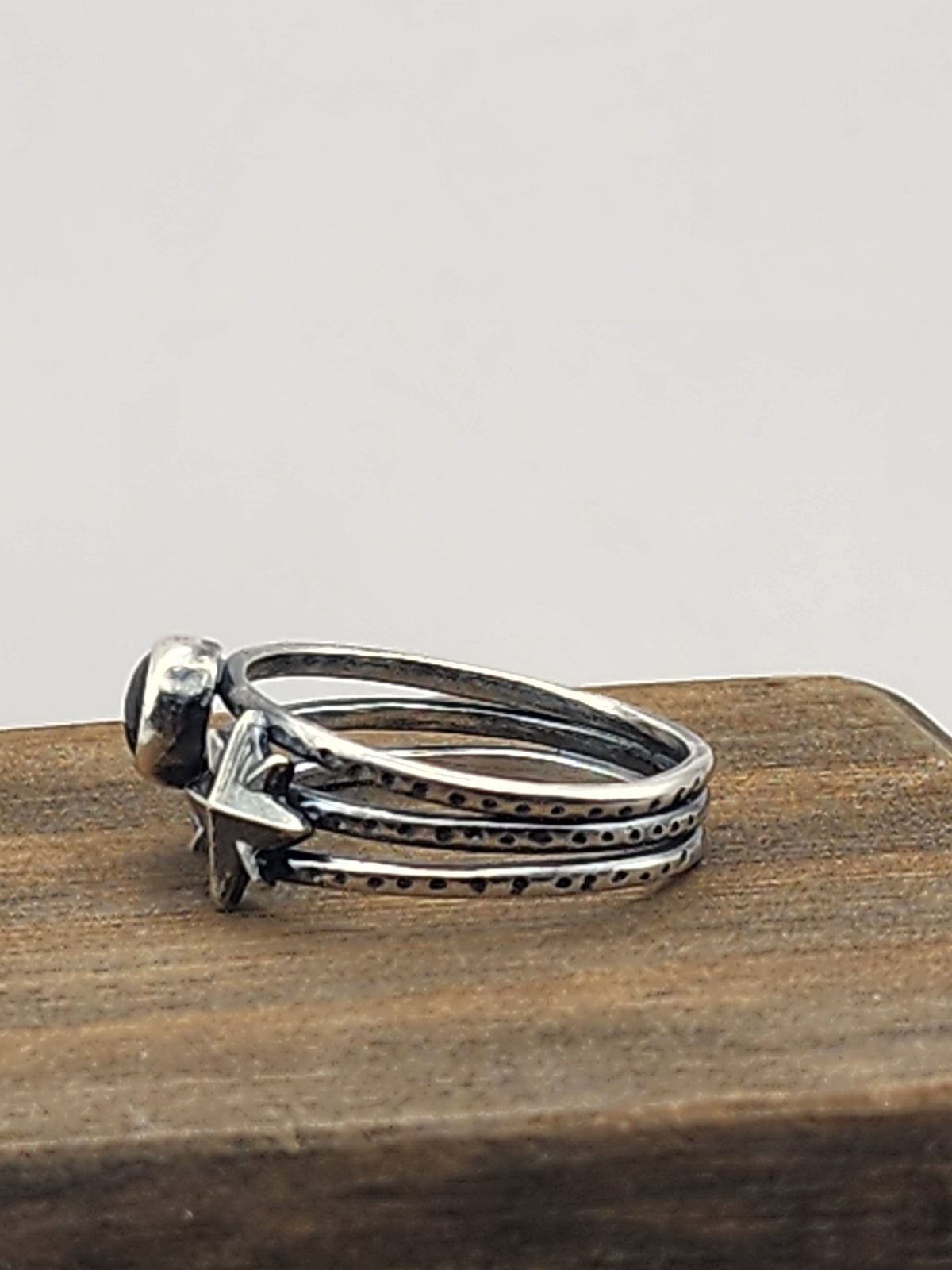 A side view of a sterling silver three-band textured ring featuring a starburst design and a round labradorite cabochon stone, displayed on a wooden block against a neutral light gray background.