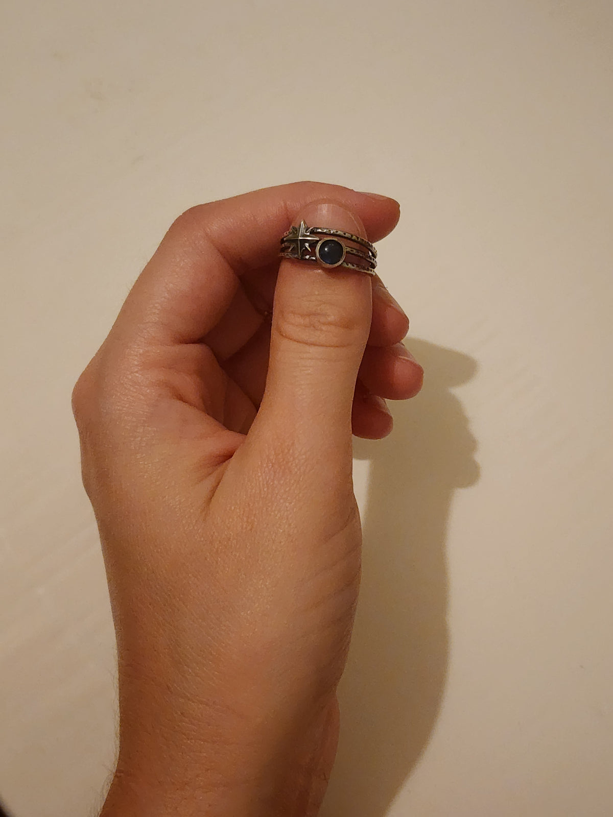 A sterling silver three-band textured ring featuring a starburst design and a round labradorite cabochon stone, positioned over a person's thumb nail with an off white background.