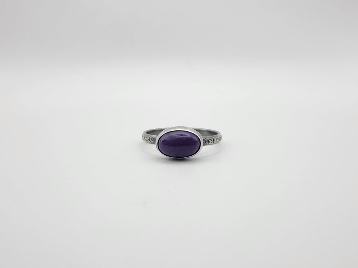 A sterling silver ring with an oval purple cabochon gemstone on a stamped ring band, photographed on a plain light gray background.