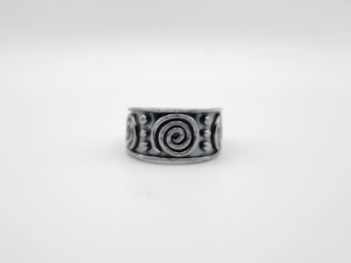 A sterling silver ring with a wide band featuring raised spiral and dot patterns, photographed against a plain light gray background.