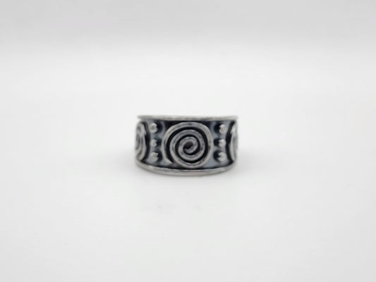 A sterling silver ring with a wide band featuring raised spiral and dot patterns, photographed against a plain light gray background.