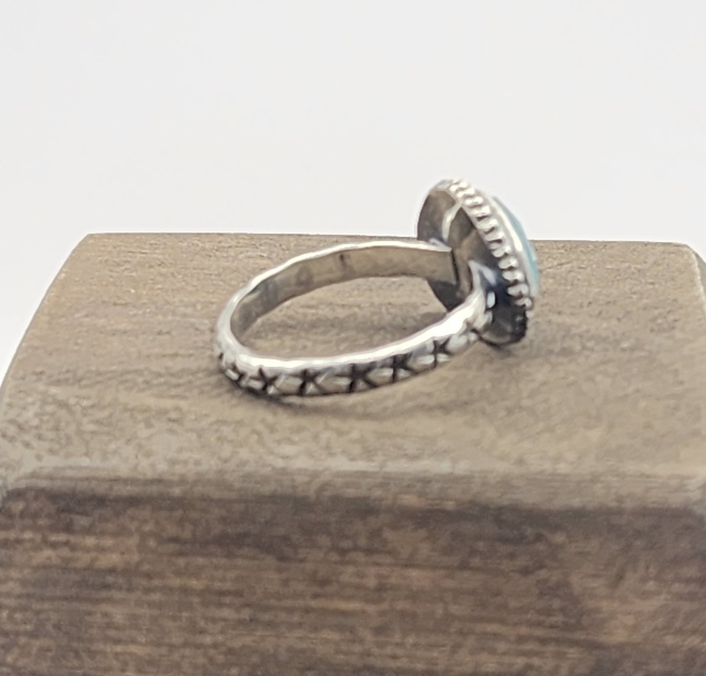 Side/back view of star stamped band of a gemstone ring on a wooden block with white background