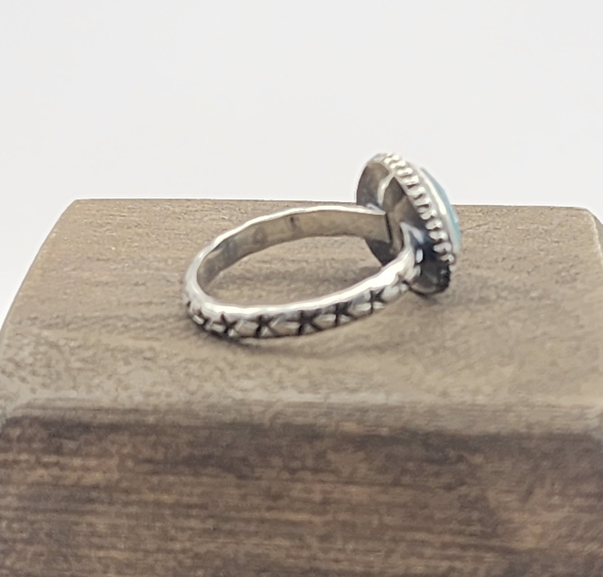 Side/back view of star stamped band of a gemstone ring on a wooden block with white background