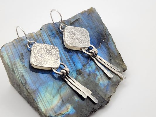 Silver dangle earrings with paddle fringes on a piece of labradorite stone and a white background