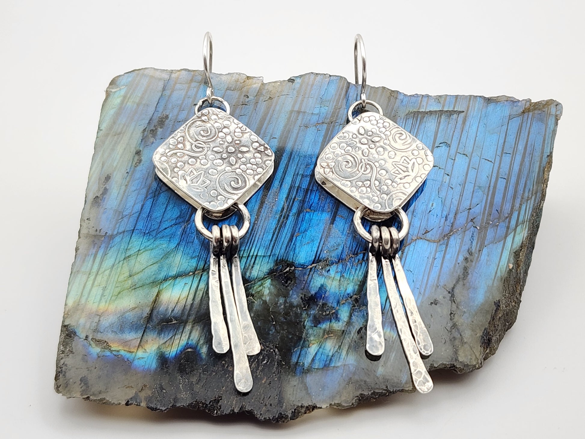 Silver earrings with dangling elements on a labradorite stone background and white background