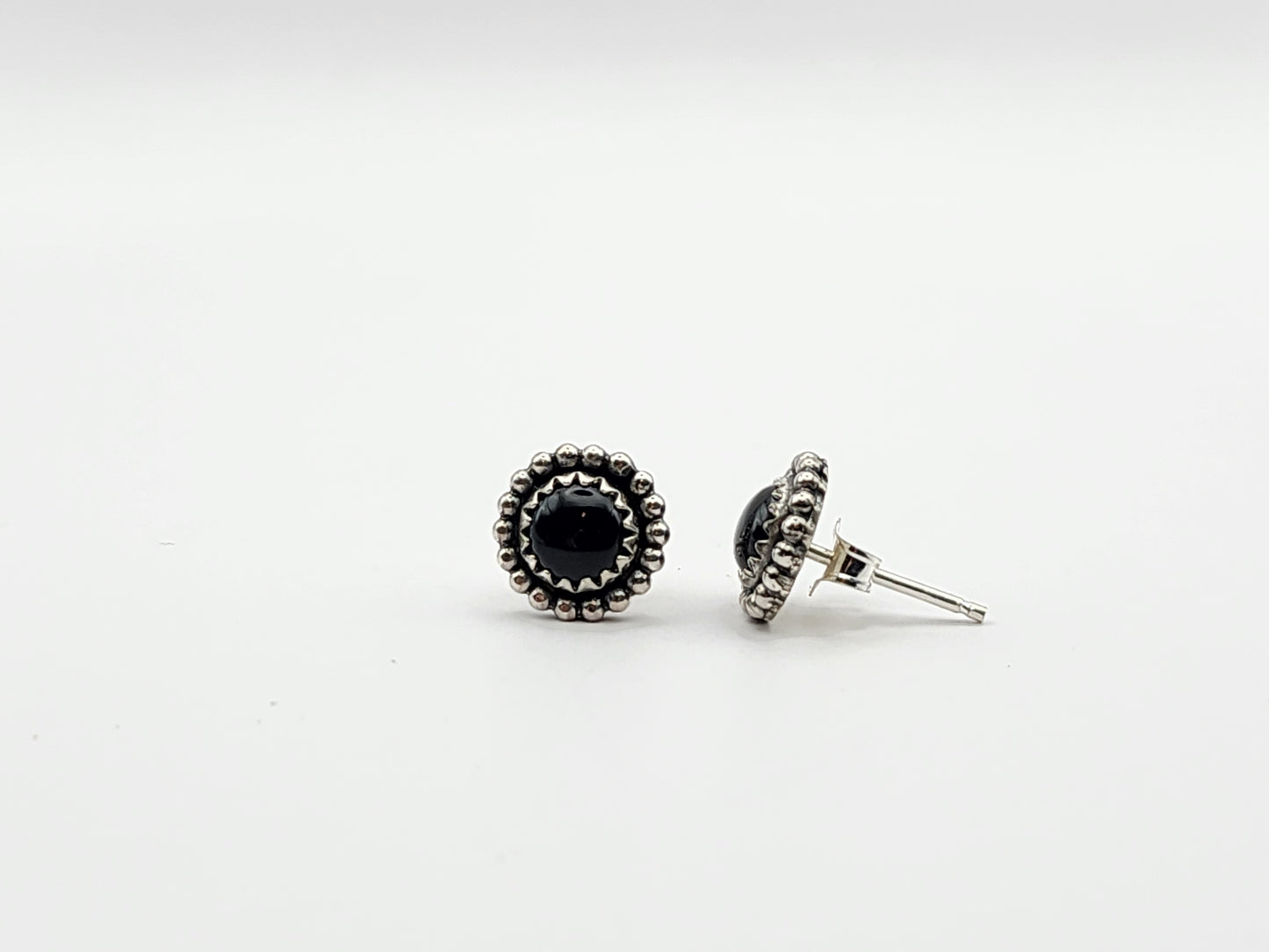 Pair of black onyx stud sterling silver earrings on a white background. One earring is turned sideways showing the post and earnut. 
