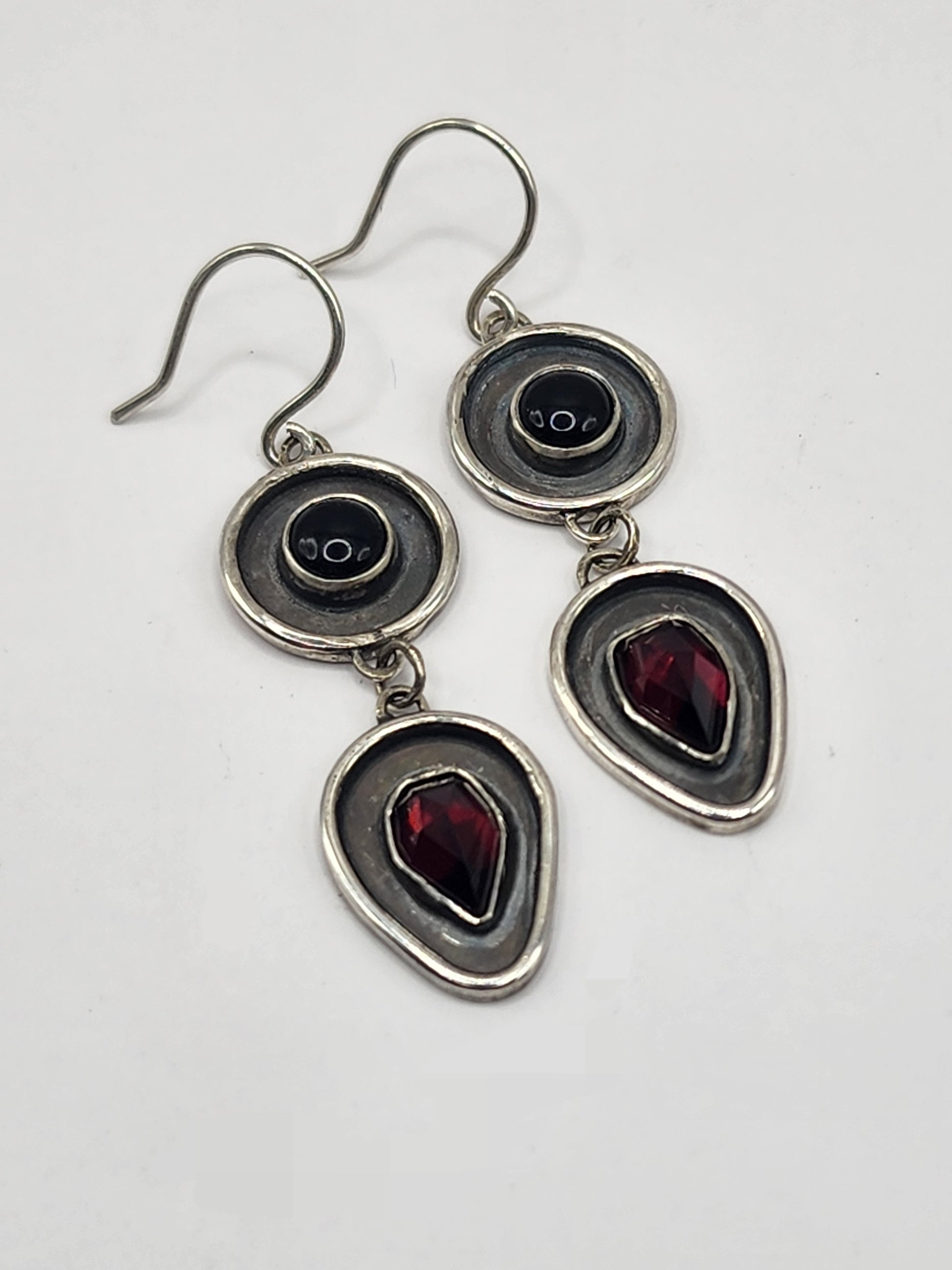 Silver earrings with black and red gemstones on a white background