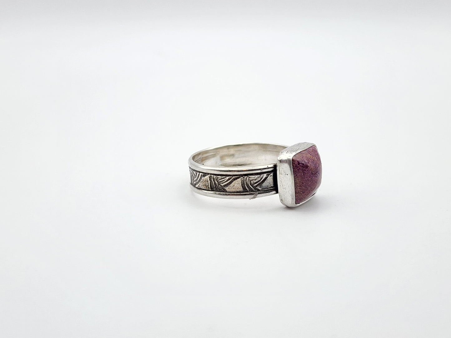Silver ring with a stichtite gemstone on a white background. side view of ring